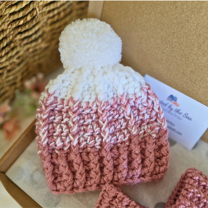 Crochet baby hat with a white pom-pom on a textured surface