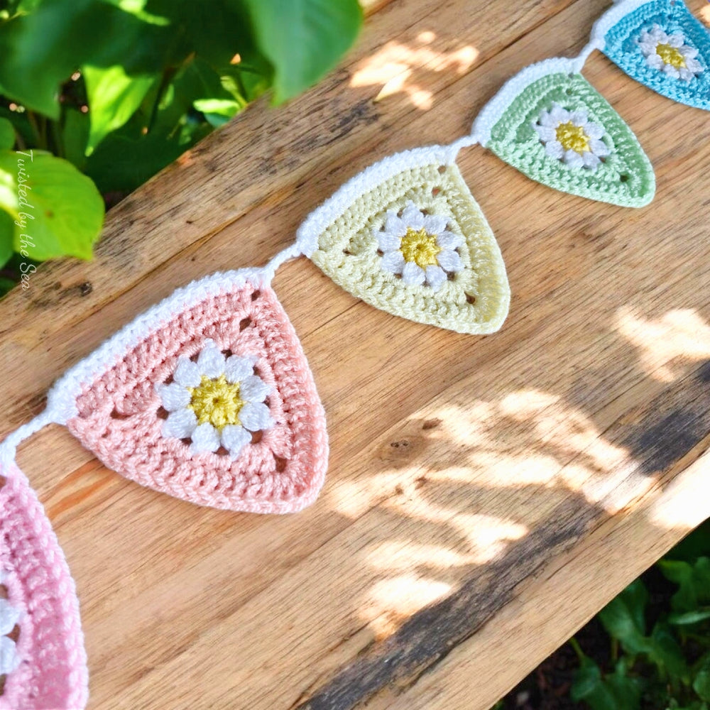 Crocheted triangle-shaped bunting with floral patterns on a wooden surface. - Twisted by the Sea 