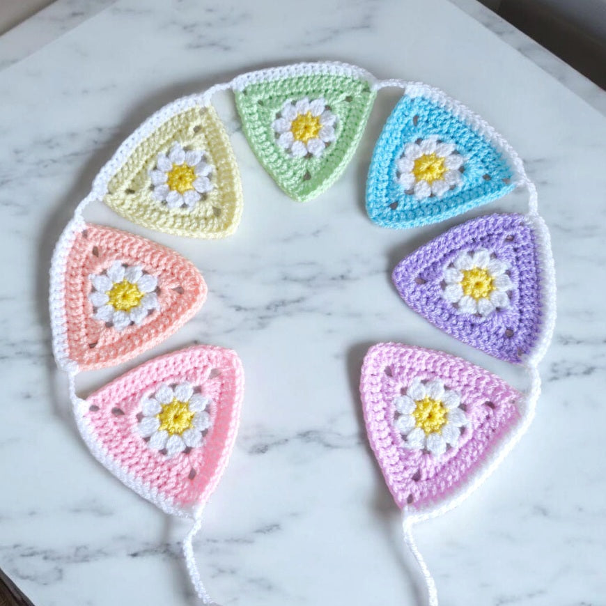 Handmade crochet rainbow bunting with seven colourful flags, made-to-order for nursery or gift on a marble counter - Twisted by the Sea 