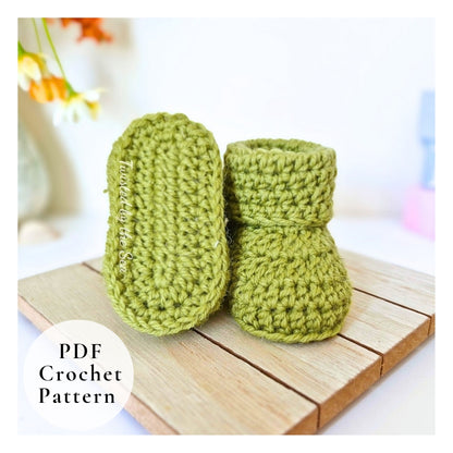 Green crochet baby booties on a wooden surface with a blurred background.