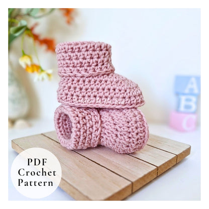 Stack of pink crochet baby booties on a wooden board with a blurred background.