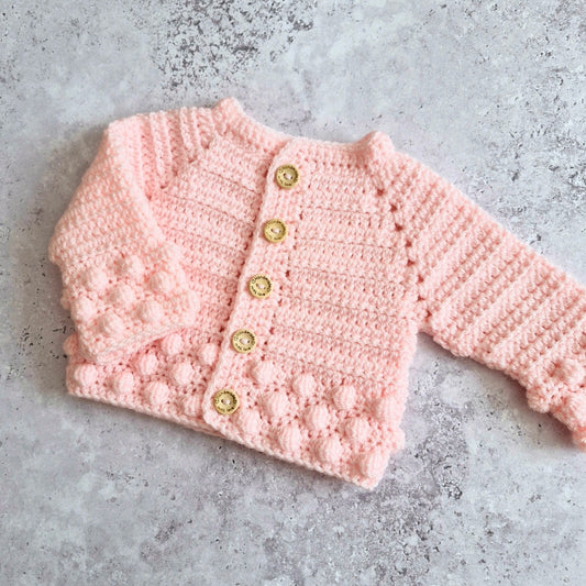 Soft peach crochet baby cardigan with wooden buttons on a gray surface