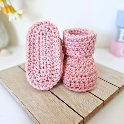 Pair of newborn candy pink crochet baby booties on a wooden surface with a blurred background