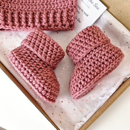 Pink crochet baby booties and hat set in a box with tissue paper.