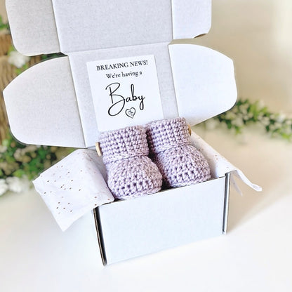 Pregnancy Announcement with baby booties and a card inside, set against a blurred natural background.