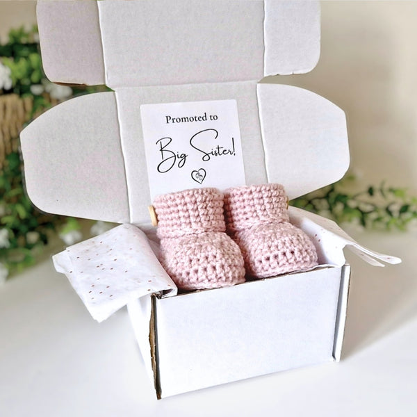 Pink baby booties and blanket in a box with 'Promoted to Big Sister!' card.