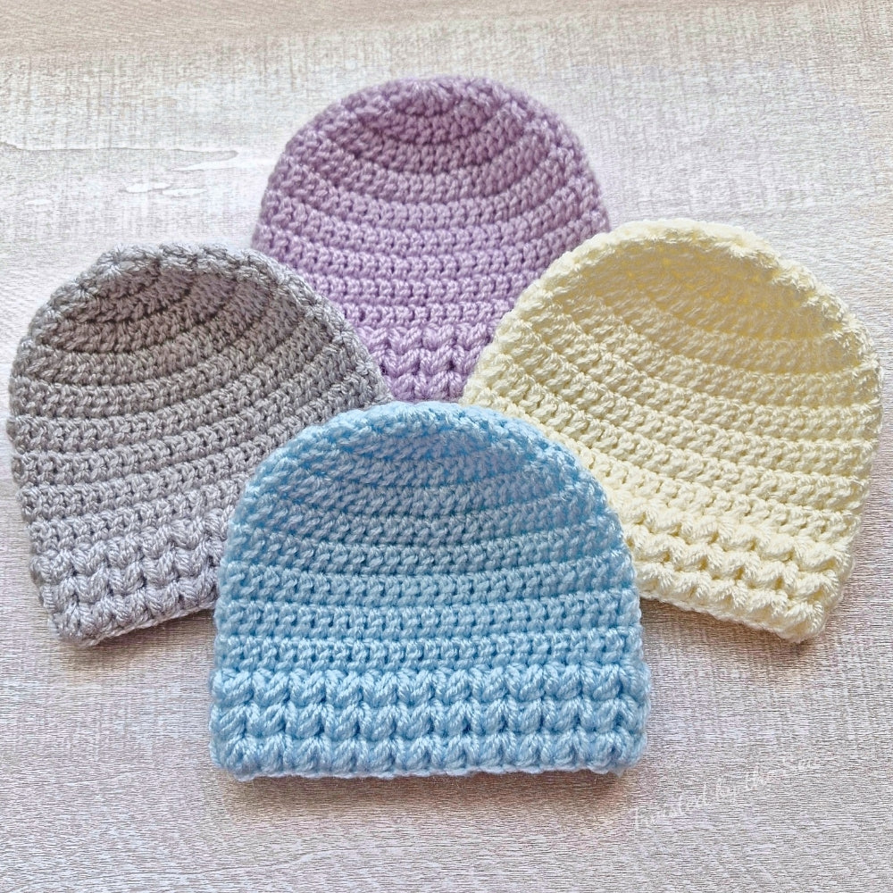 Four crocheted baby hats in different colors on a textured surface