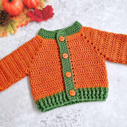 A crochet pumpkin coloured baby cardigan with leaf green edging