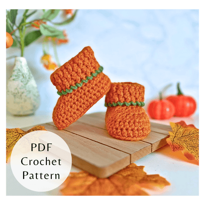 Textured orange crochet pumpkin baby booties with green leaf detail. Three-size autumn PDF pattern by Twisted by the Sea.