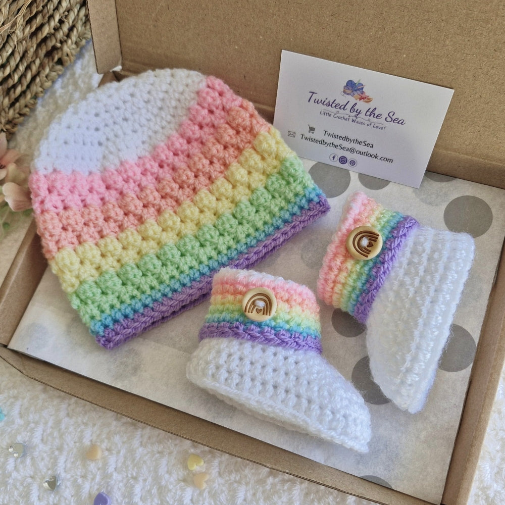 Crocheted rainbow baby hat and booties set with Twisted by the Sea branding on a cardboard box.