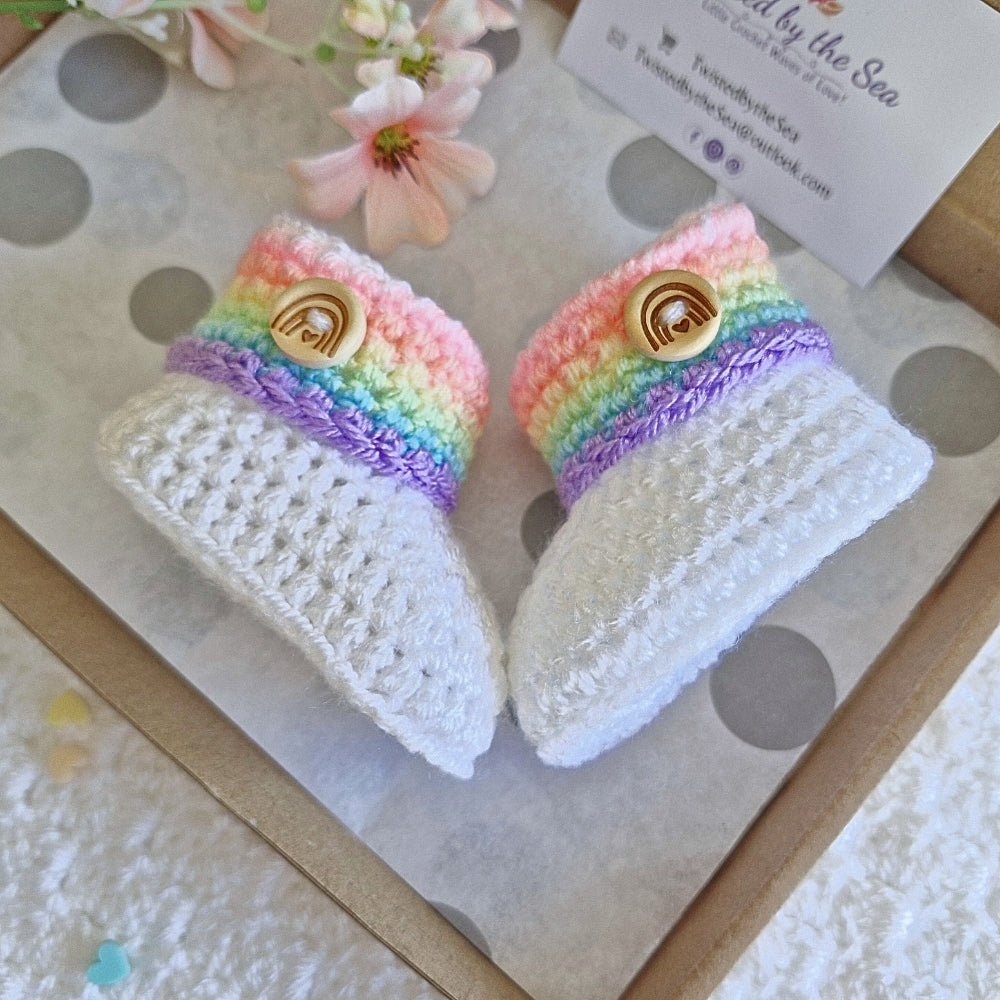 Pair of rainbow-colored baby booties with buttons on a textured surface.