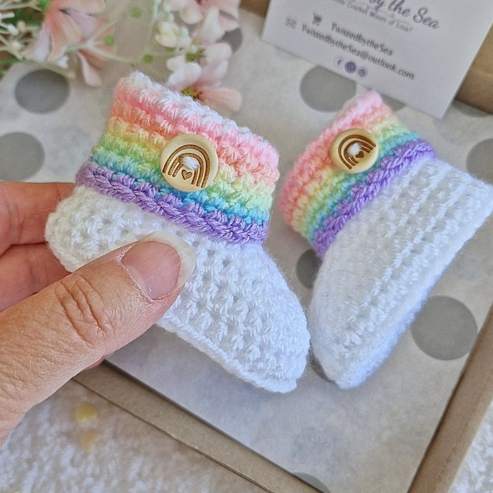 Pair of rainbow-colored baby booties with a logo on a textured surface.