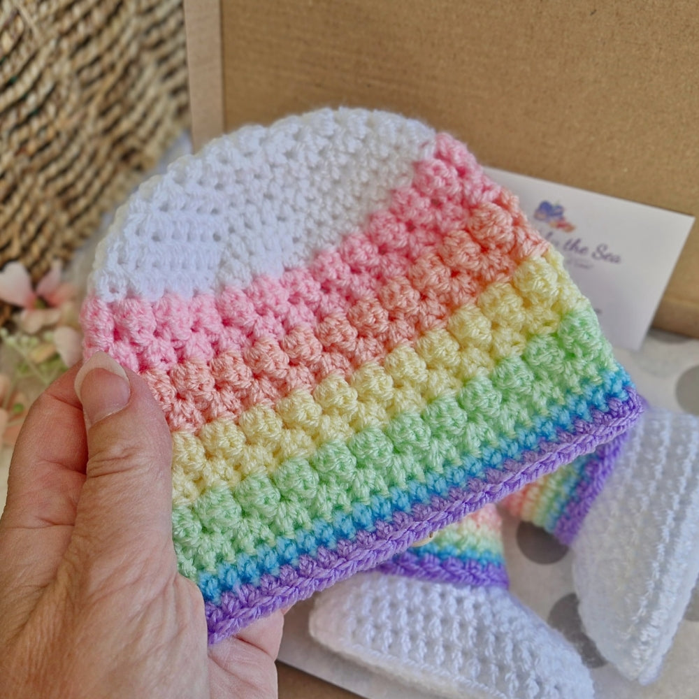 Colorful rainbow crocheted baby hat held by a hand with a blurred background