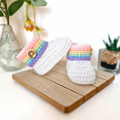 Handmade rainbow crochet baby booties with folded cuff and wooden rainbow button, displayed as a newborn gift idea