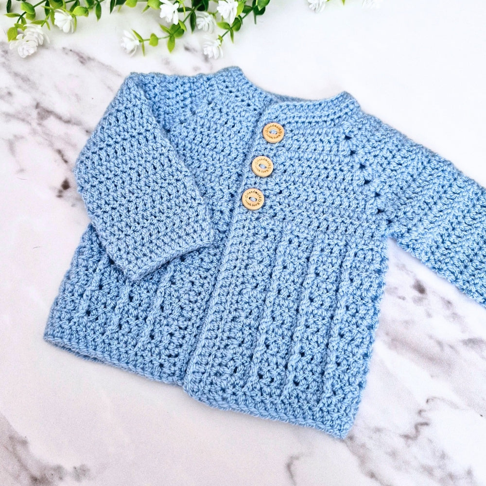 Blue crocheted cardigan with buttons on a marble surface