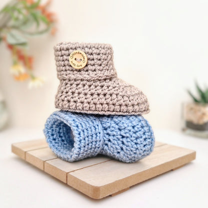 Knitted baby booties in silver and blue with a button on a wooden block
