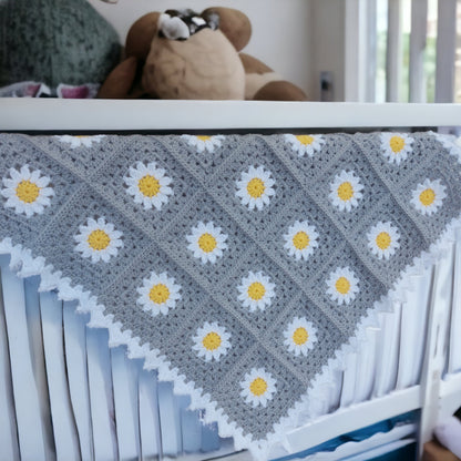 Crib with a silver blanket featuring white daisy patterns, surrounded by stuffed animals.