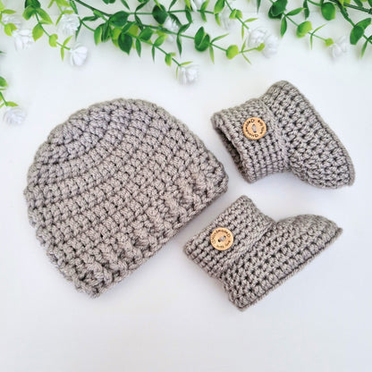 Crocheted baby hat and booties with wooden buttons on a white background with greenery.