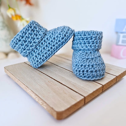 Blue crocheted baby booties on a wooden surface with a blurred background