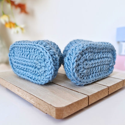 Sole view of Two blue crocheted booties on a wooden surface with a blurred background