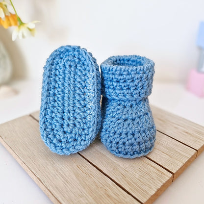 Pair of blue crochet baby booties on a wooden surface with a blurred background
