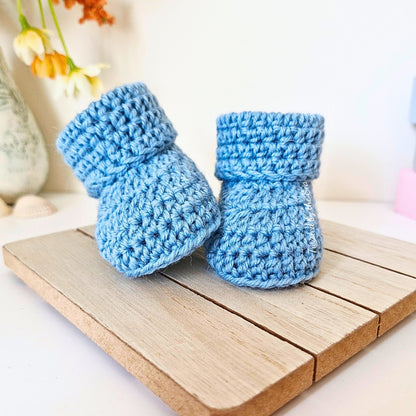 Pair of blue crocheted baby booties on a wooden surface with a blurred background
