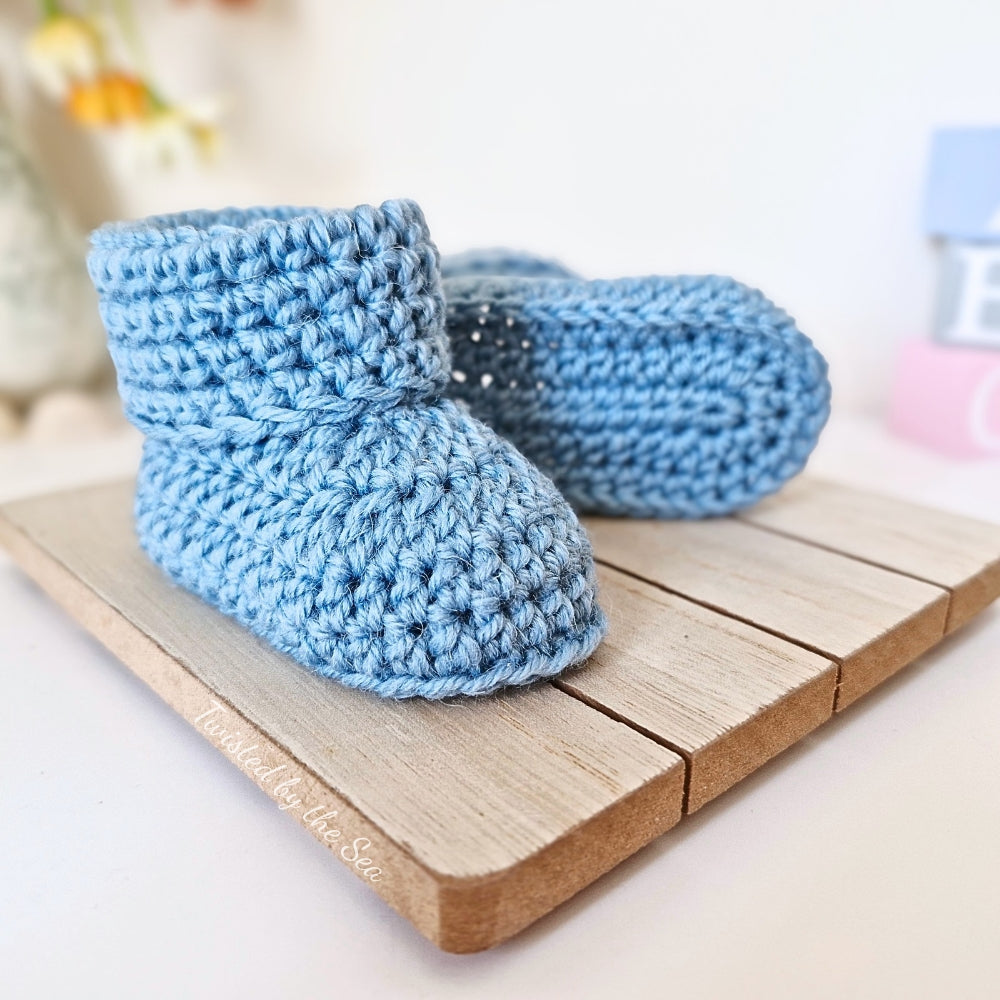 Pair of blue crochet baby booties on a wooden surface with a blurred background
