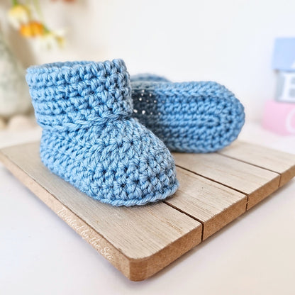 Pair of blue crochet baby booties on a wooden surface with a blurred background