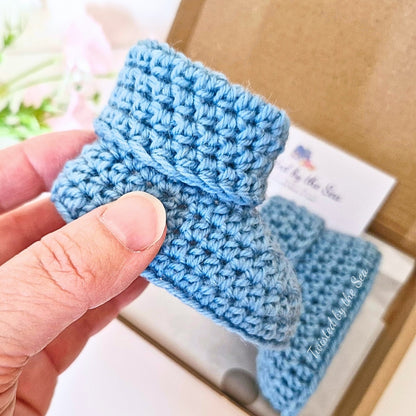Hand holding a pair of blue crochet baby booties with a blurred background