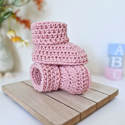 Pink crochet baby booties on a wooden surface with a blurred background