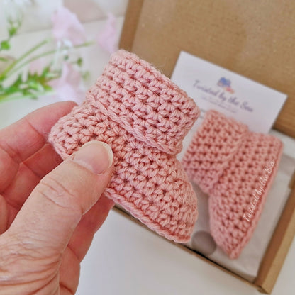 Hand holding a pink crochet baby bootie with another bootie in the background.