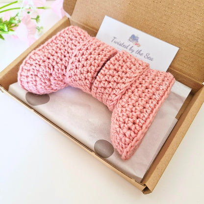 Pink knitted product in a box with a brand card on a light background