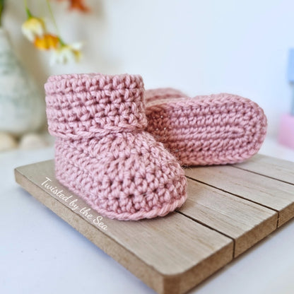 Pair of pink knitted baby booties on a wooden surface with a blurred background.