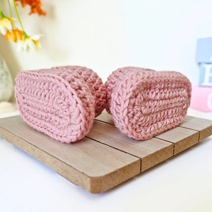 Two pink crocheted booties on a wooden surface with a blurred background