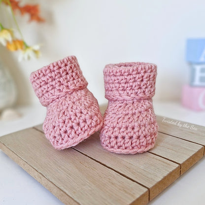 Pair of pink crochet baby booties on a wooden surface with a blurred background
