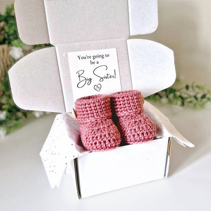 Pink baby booties in a box with a 'You're going to be a Big Sister!' card.