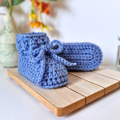 Pair of blue crocheted baby booties on a wooden surface with a blurred background