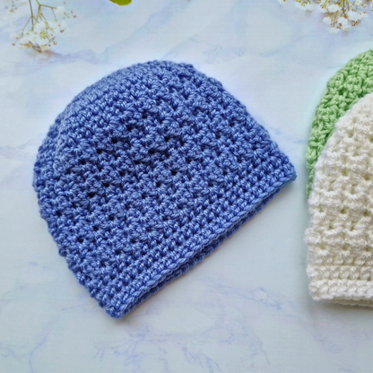 Three crocheted hats in blue, green, and white on a light marble surface.
