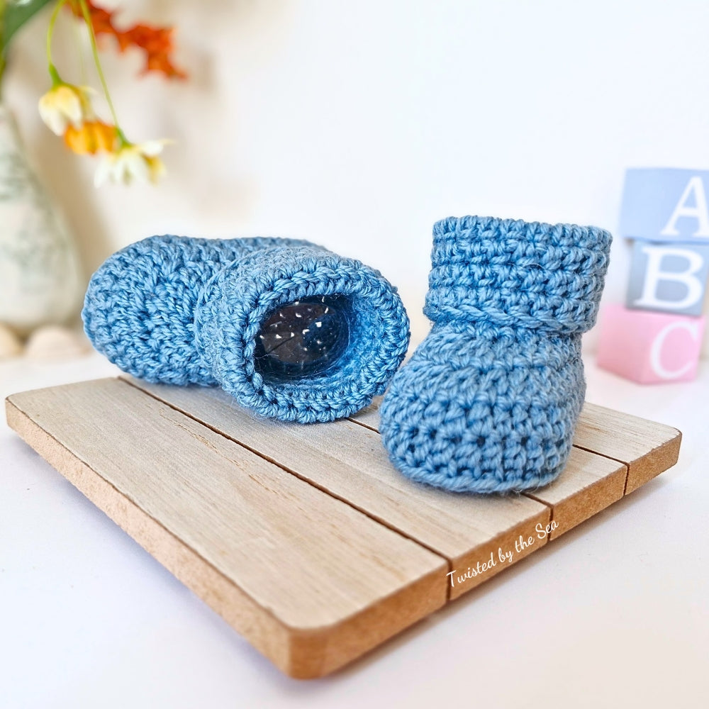 Blue crochet baby booties on a wooden block with a blurred background