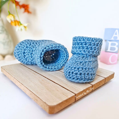 Blue crochet baby booties on a wooden block with a blurred background