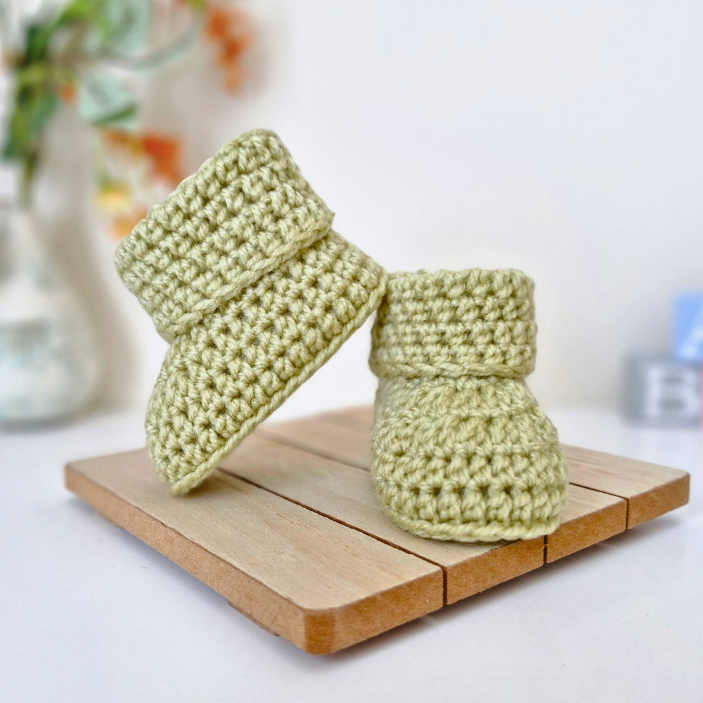 Pair of green newborn crochet baby booties on a wooden block 