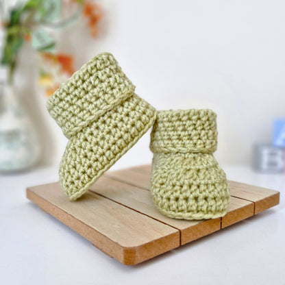 Pair of green newborn crochet baby booties on a wooden block 
