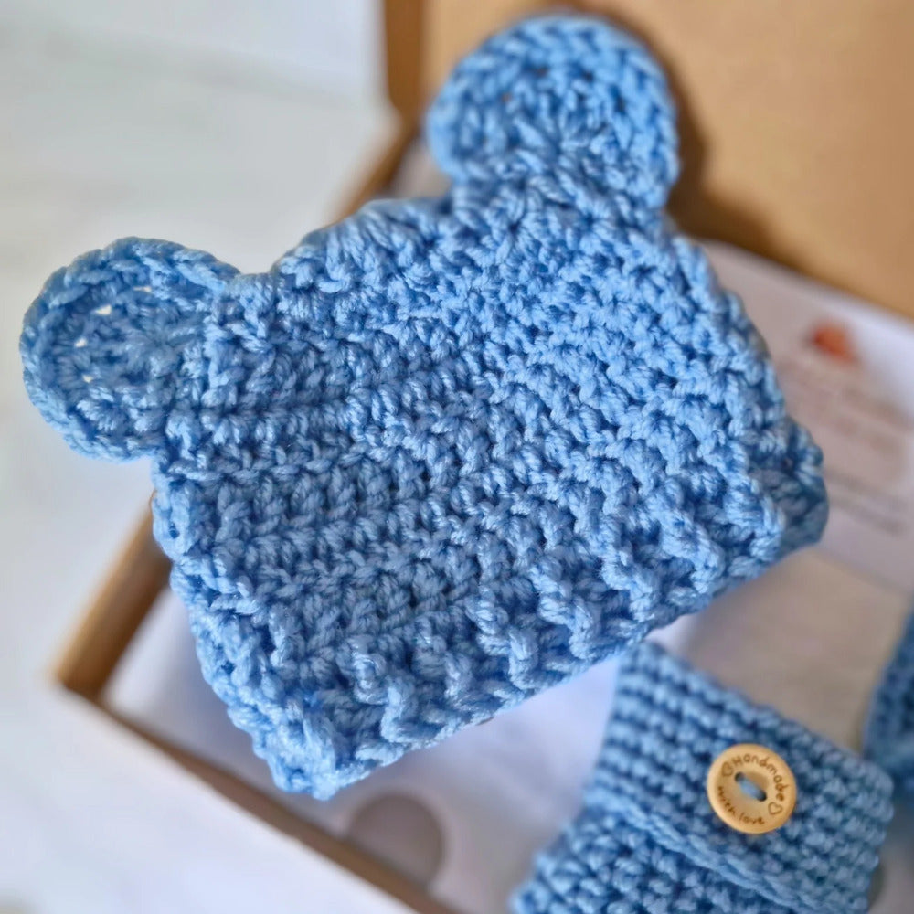 Blue knitted baby booties with a button on a white surface
