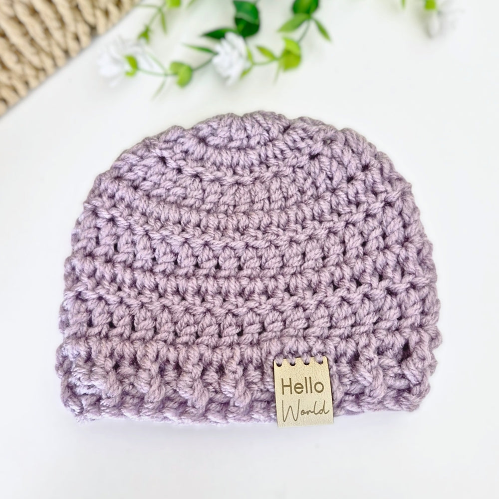 Crocheted baby hat with 'Hello World' tag on a white background