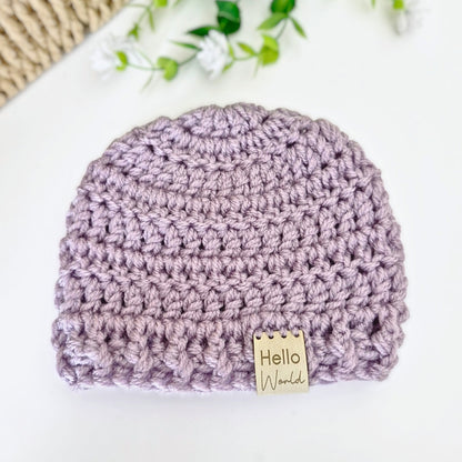 Crocheted baby hat with 'Hello World' tag on a white background