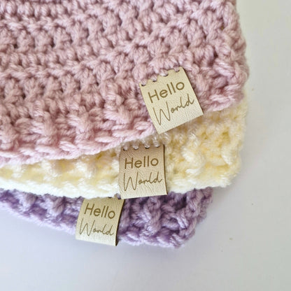 Crocheted baby hats with 'Hello World' tags on a white background