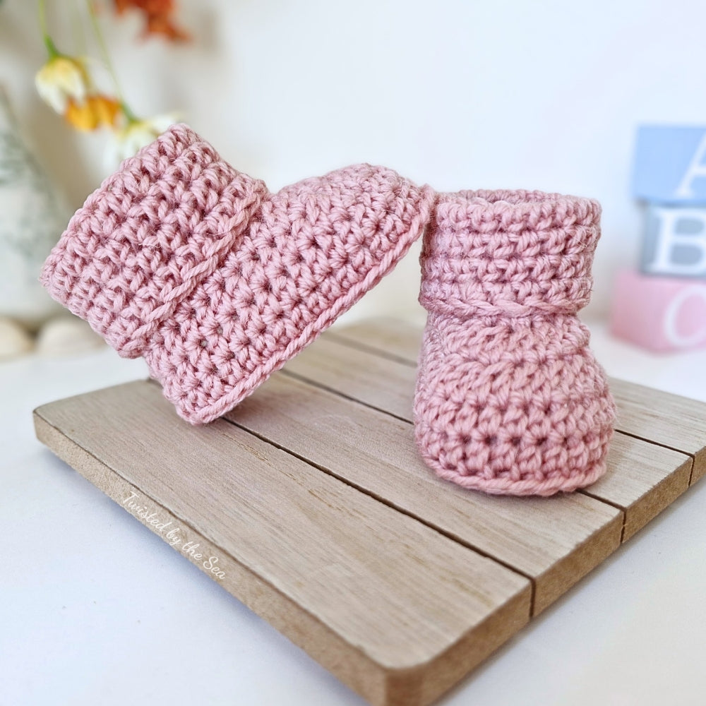 Pink knitted baby booties on a wooden board with a blurred background