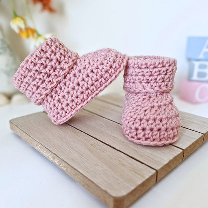 Pink knitted baby booties on a wooden board with a blurred background