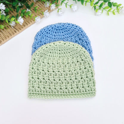 Two crocheted beanies, one green and one blue, on a white surface with decorative elements.