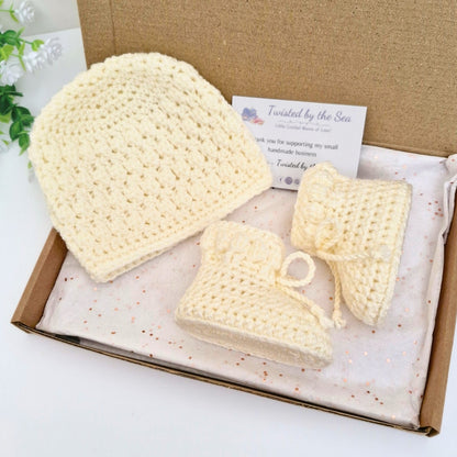 Set of cream crocheted baby hats in a box with a card on a white background